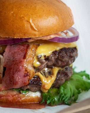 İki köfteli büyük lezzetli et burgeri. Kızarmış pastırma. Peynir ve yeşil salata. Tahta tabakta hamburger. Kafeler ve restoranlar için menü. Makro.