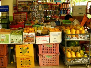 01 Haziran 2008: Fruit stall, Singapur, arka raflarda çeşitli taze meyve çeşitleri ve önceden paketlenmiş hazır atıştırmalıklar sergileniyor. Genç bir erkek asistan günlük stok kağıtları üzerinde çalışıyor.