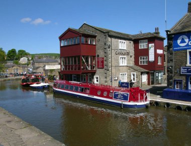 11 Mayıs 2009: İngiltere 'de Skipton, Yorkshire' daki Canal Side barının bitişiğindeki Leeds Liverpool kanalına demirlemiş kırmızı dar tekne. Uzakta, diğer benzer tekneler kayıkhanenin yanında demirli.