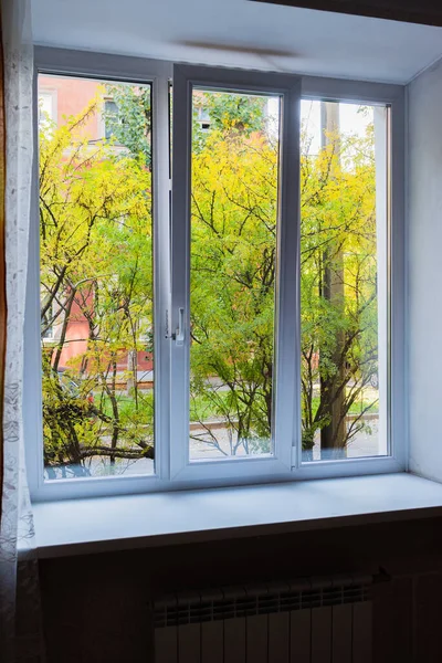 Yeşil ağaçlar ve kırmızı bir evin beyaz plastik penceresinden görüntüsü