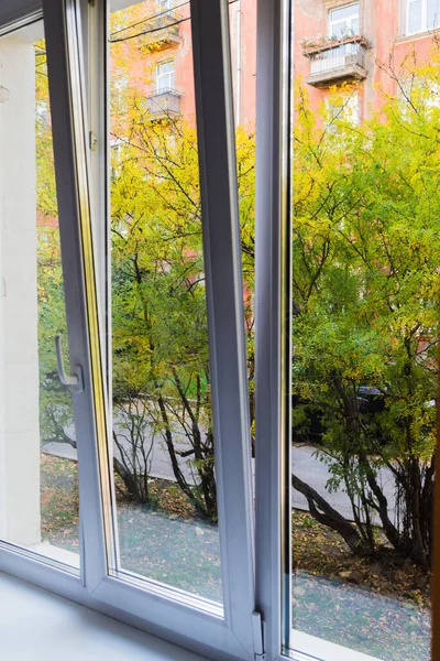 Yeşil ağaçlar ve kırmızı bir evin beyaz plastik penceresinden görüntüsü