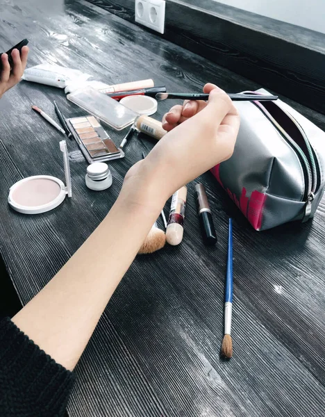 Model fotoğraf çekiminden önce makyaj uygular. Stüdyoda çeşitli kozmetik ürünler masanın üzerinde yatar.