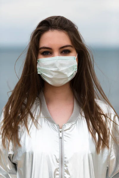 Tıbbi maskeli, kahverengi saçlı ve gümüş renkli ceketli bir kızın portresi.