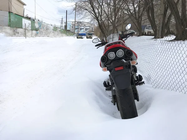Red motorcycle stands in a snowy parking lot covered in snow in winter