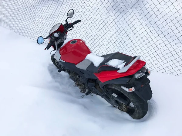 Red motorcycle stands in a snowy parking lot covered in snow in winter