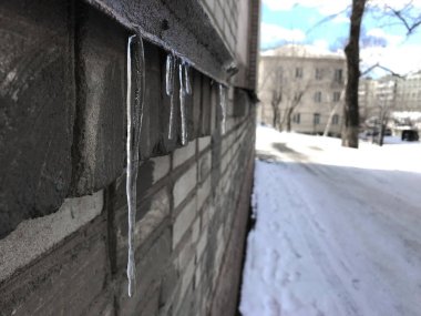 Buz saçakları yolun yanındaki gri binanın güneşliğinde asılı, bahar buzları eriyor.