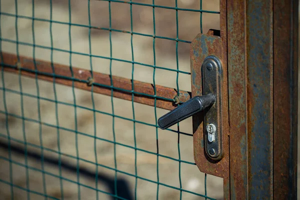 Ржавая дверь, ворота закрыты на ручку-замок с металлической сеткой на улице — стоковое фото