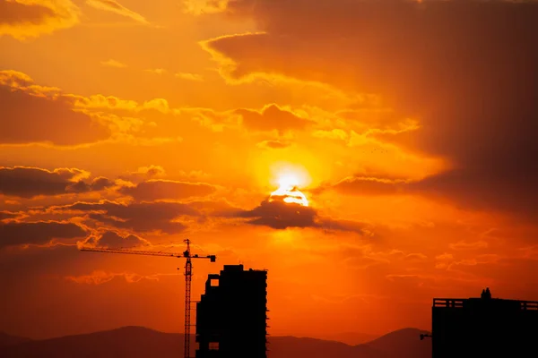 Construction crane at sunset on a background of orange sun, a city by the sea — Stock Photo, Image