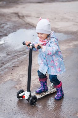 Küçük kız yağışlı yolda kick scooter üzerinde sürüş