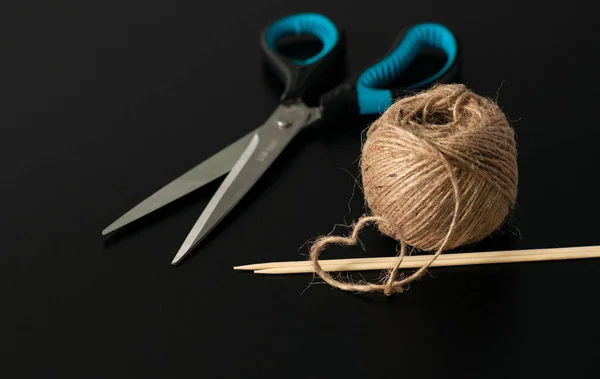 yarn, scissors and wooden knitting needles on a black background