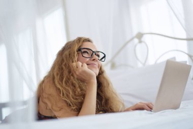 Genç kadın yatakta dizüstü bilgisayar ile rahatlatıcı