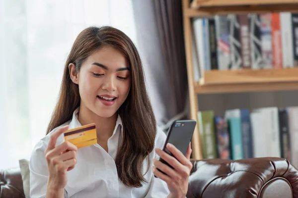 Mujer asiática joven sosteniendo la tarjeta de crédito y el uso de teléfono móvil, En —  Fotos de Stock