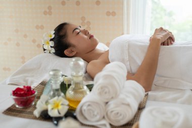 Genç Asyalı kadın masaj yatağında uzanıyor, spa salonunda dinleniyor.