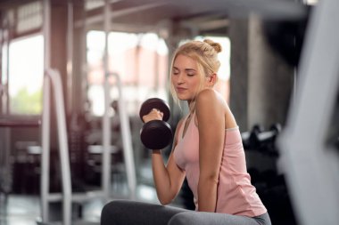 Güçlü kadın dambıllarla çalışıyor, spor salonunda egzersiz yapıyor.