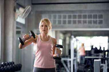 Güçlü kadın dambıllarla çalışıyor, spor salonunda egzersiz yapıyor.