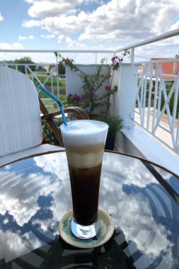 Balkonda ılık bir bahar gününde, uzun bir bardakta soğuk kahve..