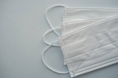 Açık mavi arka planda izole edilmiş üç beyaz tıbbi maske.