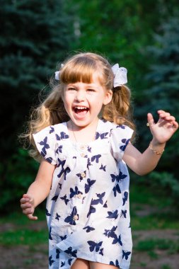 Beyaz elbiseli bir kız parkta koşuyor ve gülüyor.