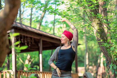 Kırmızı sarıklı bir kadın parkta dikiliyor. Yoga Mudra 'da elinizi kaldırın..