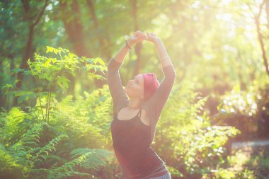 Kadın gün batımında yoga pozisyonunda duruyor. Güneş ışığı sisi. Eller havaya. Başka tarafa bakıyor. arkaya doğru eğil.
