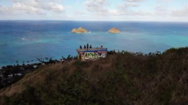 Lanikai Pillbox, Oahu, Hawaii, ABD 'de sahil, palmiye ağaçları ve köylü turkuaz kıyı şeridine bakan insanların bulunduğu 4K insansız hava aracı görüntüleri..