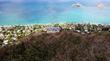 Lanikai Pillbox, Oahu, Hawaii, ABD 'de sahil, palmiye ağaçları ve köylü turkuaz kıyı şeridine bakan insanların bulunduğu 4K insansız hava aracı görüntüleri..