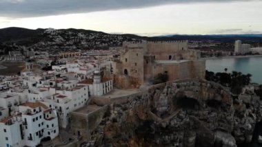 Peiscola, Castelln, Spain.Orta açı, parallax hareket alanındaki uçurum kıyısındaki eski kasaba ve kale üzerinde 4K gün batımı drone görüntüleri.