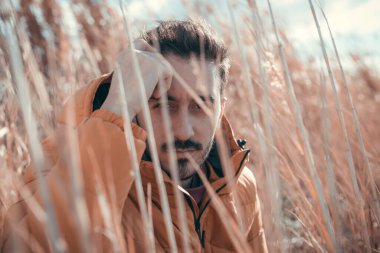 Tarlada oturan beyaz bir adam. Sarı örtülü ceket. Güneşli bir gün