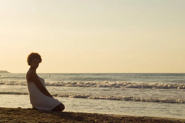 African American black woman thinking on the beach in the sunrise with a white dress