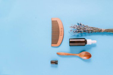 Ahşap kaşık, fırça ve lavanta ile mavi arka planda izole edilmiş gerekli yağ şişesi