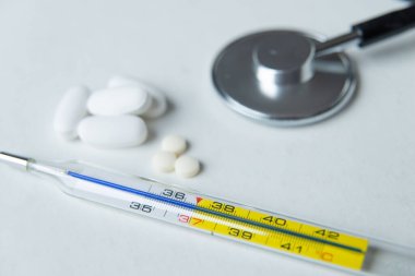 Beyaz masada termometre, steteskop ve ilaç.