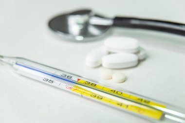 Beyaz masada termometre, steteskop ve ilaç.