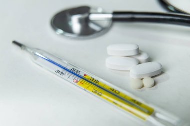 Beyaz masada termometre, steteskop ve ilaç.