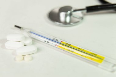Beyaz masada termometre, steteskop ve ilaç.