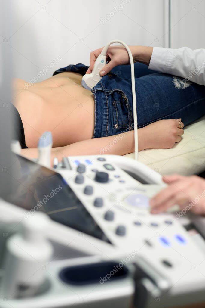 Female doctor working with ultrasound scanner examining her patient's belly in a modern clinic.