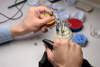 Elinde burs, cilalama ve matkapla bir diş matkabı tutan bir teknisyenin yakın çekimi ve laboratuarda takma dişler oluşturmak için çalışıyor..