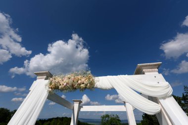 Güzel bir gökyüzüne karşı çiçeklerle süslenmiş bir düğün töreninde beyaz kemer..