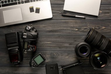 Serbest fotoğrafçı çalışma alanının en üst görüntüsü. DSLR kamera, laptop, flaş, kablosuz tetik, grafikler tablet ve fotoğraf aksesuarları koyu ahşap bir masa üzerinde..