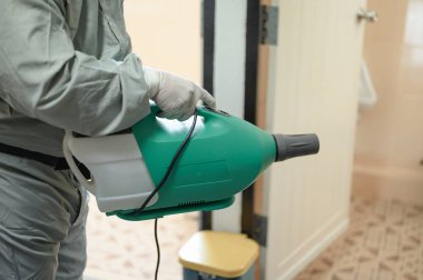 COVID-19 'u önlemek için ofisin dezenfekte edilmesi, ofiste dezenfekte edilmiş beyaz tehlikeli madde giysisi giyen kişi koruyucu maske takıyor ve Coronavirus püskürtüyor..