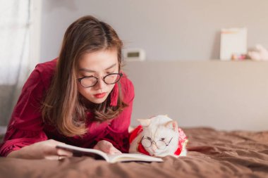 Asyalı kadınlar evde kedileriyle yatakta kitap okuyor, evde dinleniyorlar..