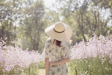 Sırtı ve çiçek tarlasında hasır şapkası olan mutlu Asyalı kadın çiçek tarlasında eğleniyor ve doğanın tadını çıkarıyor..