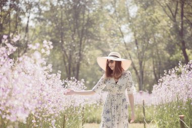 Sırtı ve çiçek tarlasında hasır şapkası olan mutlu Asyalı kadın çiçek tarlasında eğleniyor ve doğanın tadını çıkarıyor..