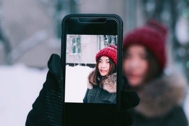 Erkek adam kışın akıllı telefon kamerasıyla kadının fotoğrafını çekiyor.