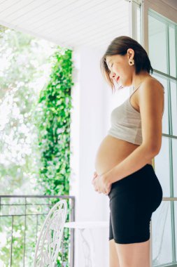 24 haftalık hamile kadın yatak odasındaki pencerenin yanında dinleniyor.