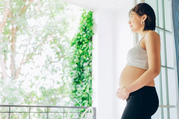 24 Weeks pregnant woman relaxing near window at home in bedroom