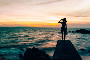 Genç bir kadın gün batımında, yaz tatilinde sahilde duruyor..