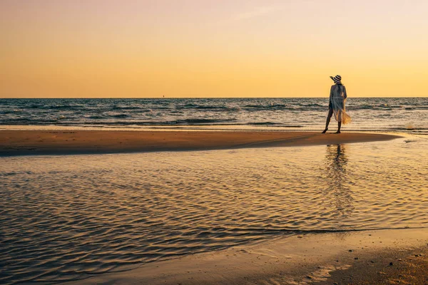 Genç bir kadın gün batımında, yaz tatilinde sahilde duruyor..