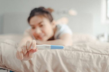 Genç Asyalı kadın hamilelik testine bakıyor. Hamilelik aile konsepti.