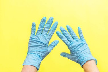 Sarı arka planda tek kullanımlık nitril eldivenli kadın elleri. Koronavirüs koruması kavramı, COVID-19 salgını, küresel karantina.