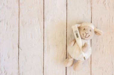 Hafif ahşap arka planda termometresi olan oyuncak kuzu. Soğuk algınlığı ve grip. Üst manzara, düz kompozisyon. Metin için alanı kopyala.